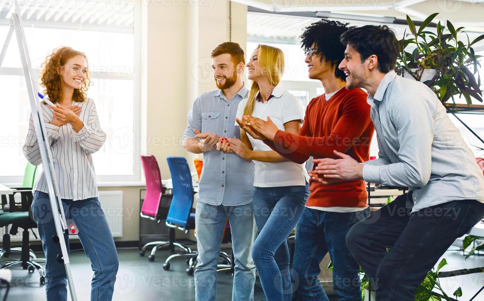 A multiracial team engages in a collaborative exercise, fostering teamwork and camaraderie. They appear to be enjoying a playful moment, clapping and smiling, possibly celebrating a milestone photo