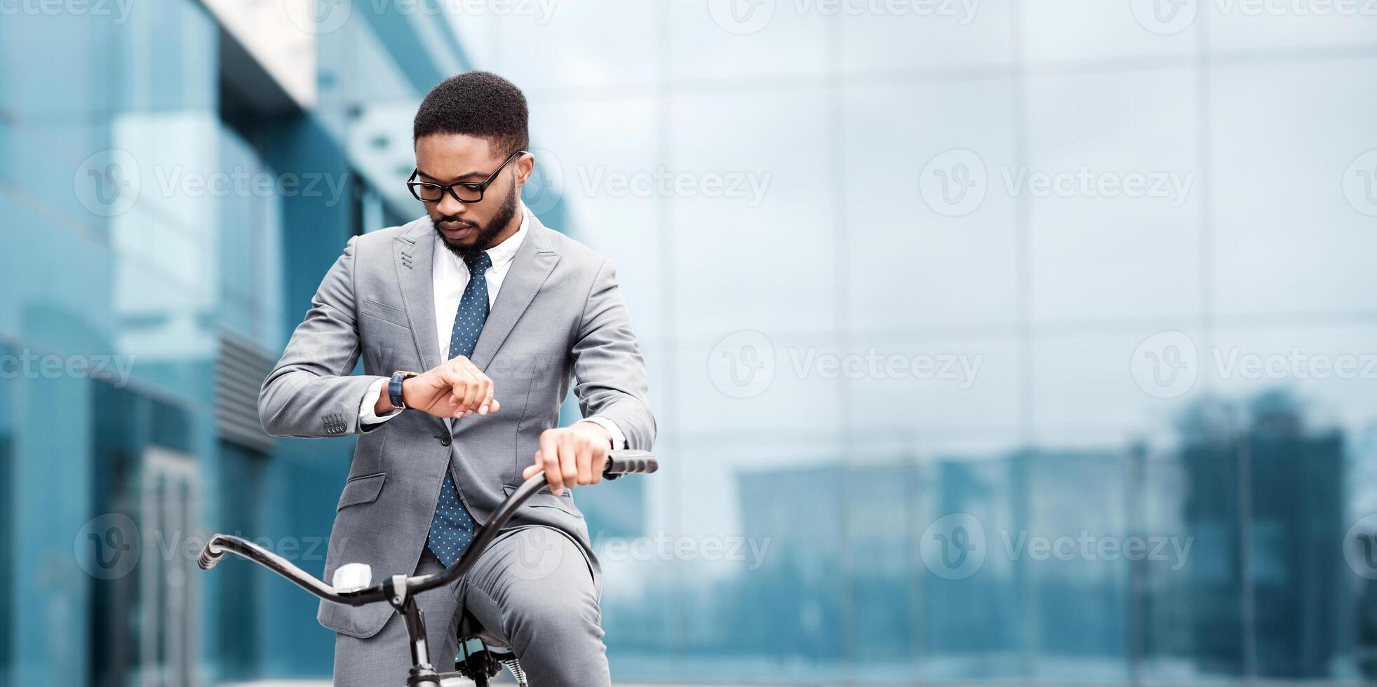 Black man professional commuting by bike is checking the time in an urban environment. The atmosphere is vibrant and hectic, reflecting the fast-paced nature of city life and work. photo