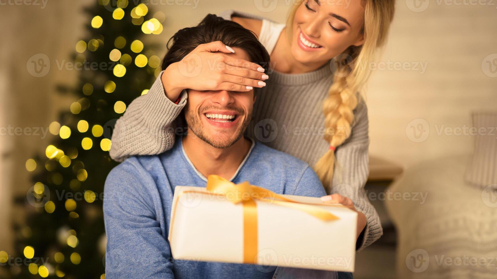 Happy woman surprising husband with Christmas gift, spending time at home together photo