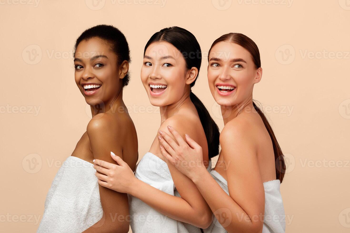 Three Happy Diverse Women Posing In Bath Towels Standing Over White Background. Studio Shot photo