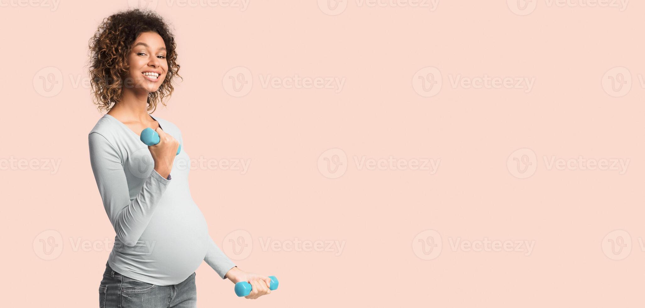 Pregnancy fitness. African-american pregnant girl exercising with dumbbells over white background, panorama with copy space photo