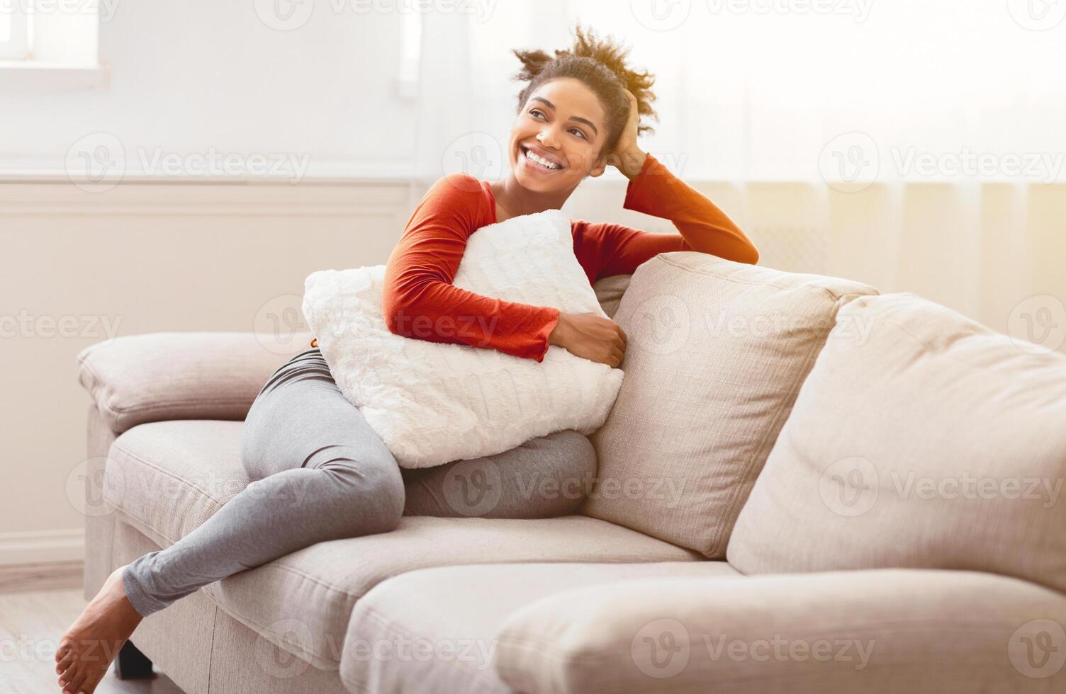Weekend. Cheerful Black Girl Sitting On Couch Hugging Pillow Relaxing At Home On Weekend Morning. Empty Space photo