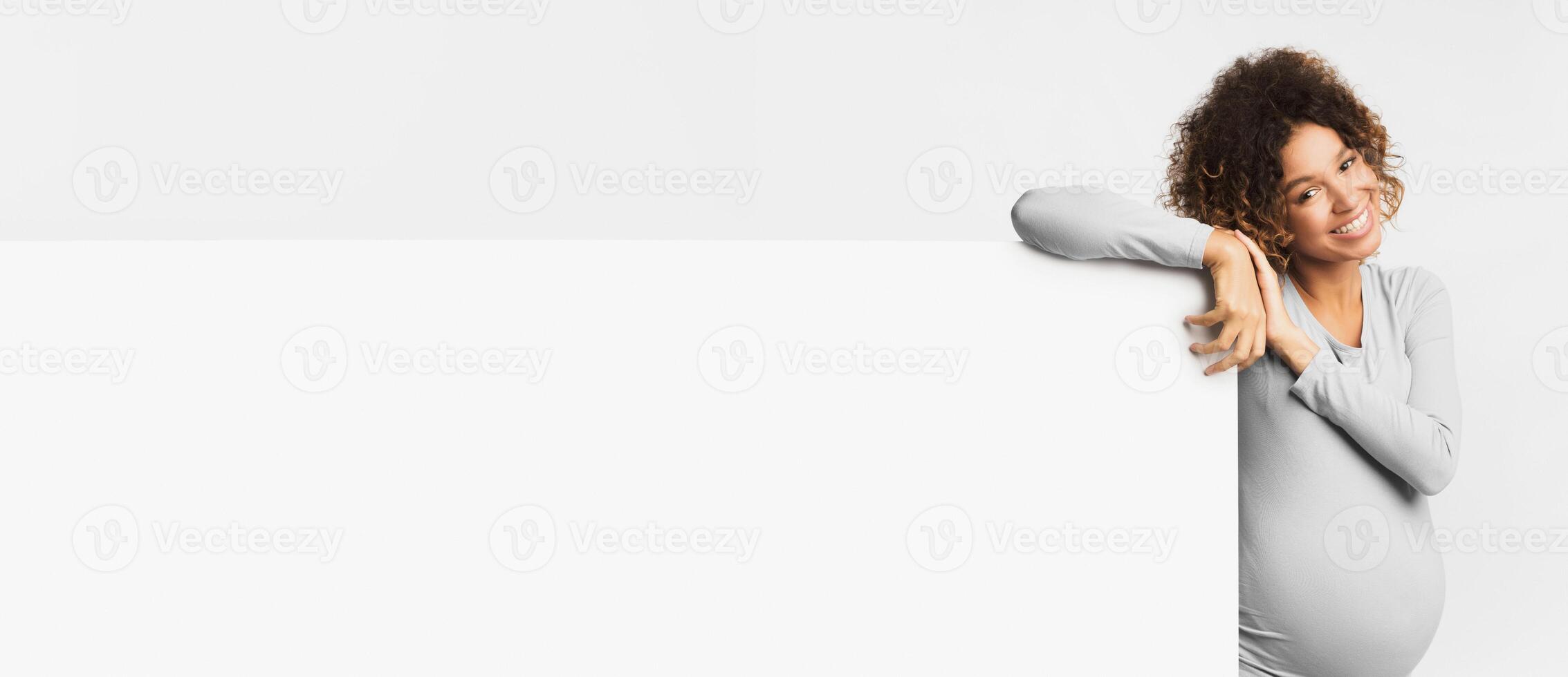 Happy black pregnant woman with empty billboard on light background, copy space photo