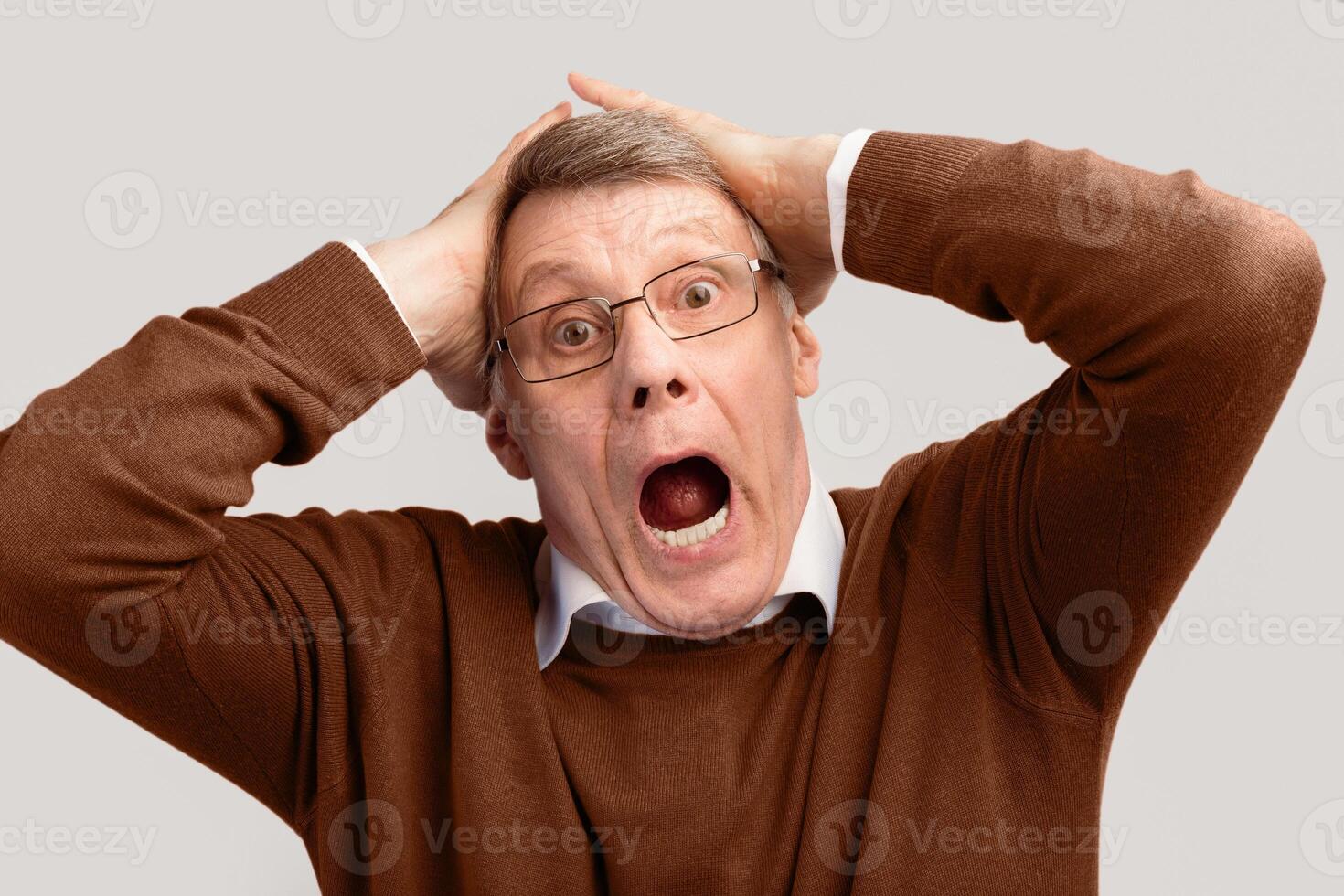 Shocked Elderly Man Shouting Clutching Head Looking At Camera Standing Over Gray Background. Stress Concept. Studio Shot photo