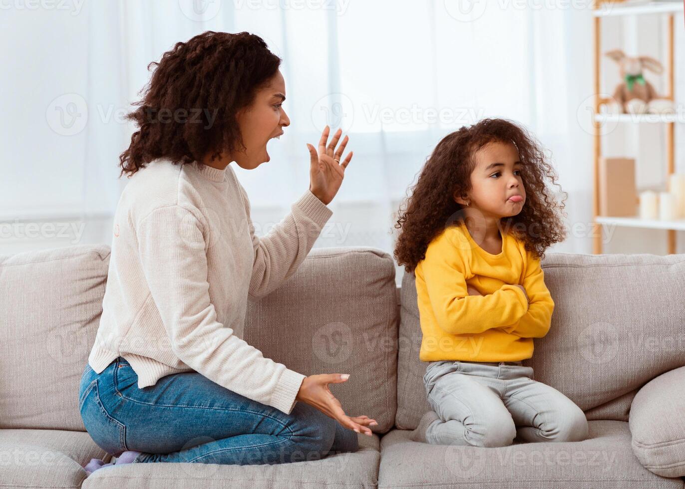 Angry Afro Mother Shouting At Offended Daughter Sitting On Couch At Home. Family Problems, Quarrels And Aggression photo