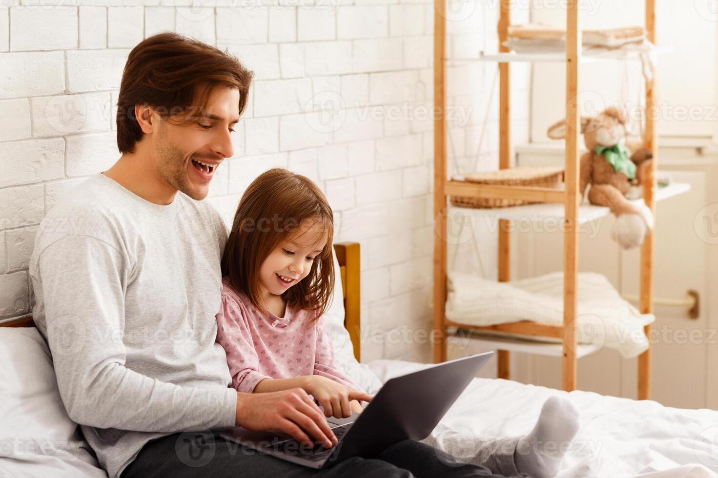 Preschool girl spending time with her daddy on weekend at home, using laptop in bedroom, copy space photo