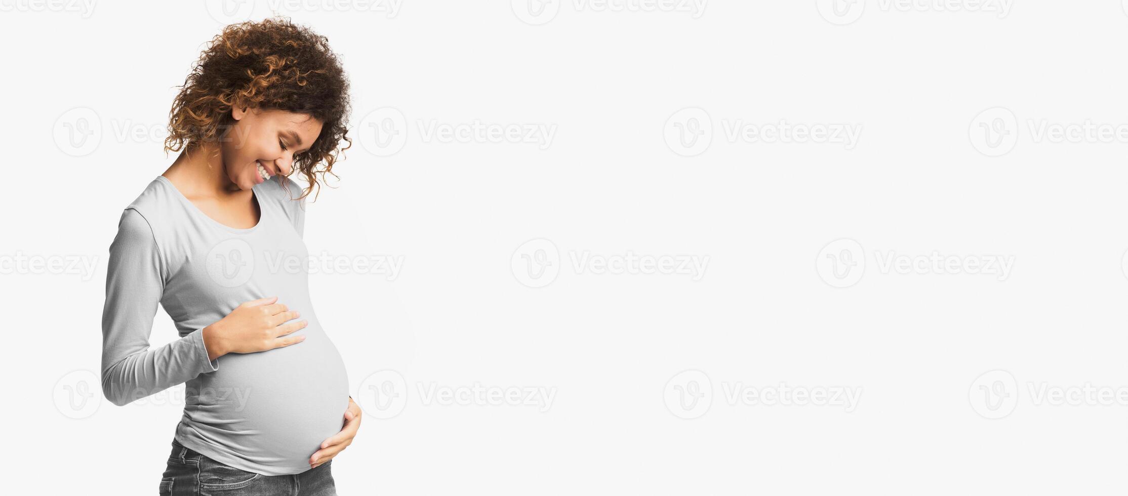 Afro woman feeling unity with unborn child, touching her belly, white background photo