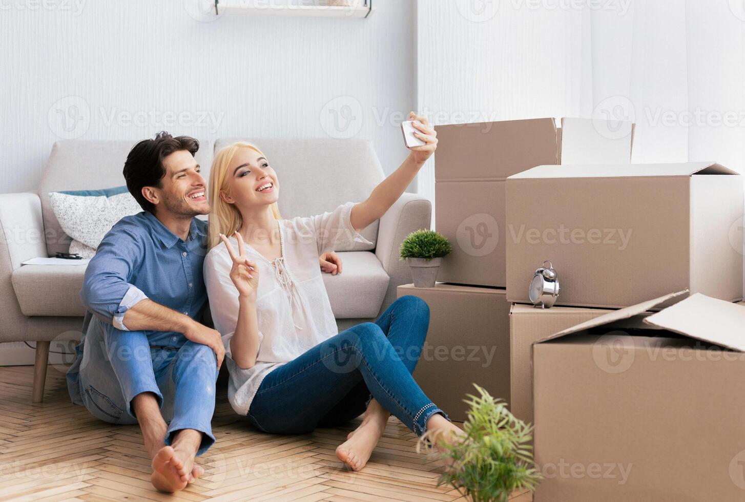 Happy House Owners. Couple Taking Selfie With Smartphone Gesturing Victory Sign After Moving Into New Home. Copy Space photo