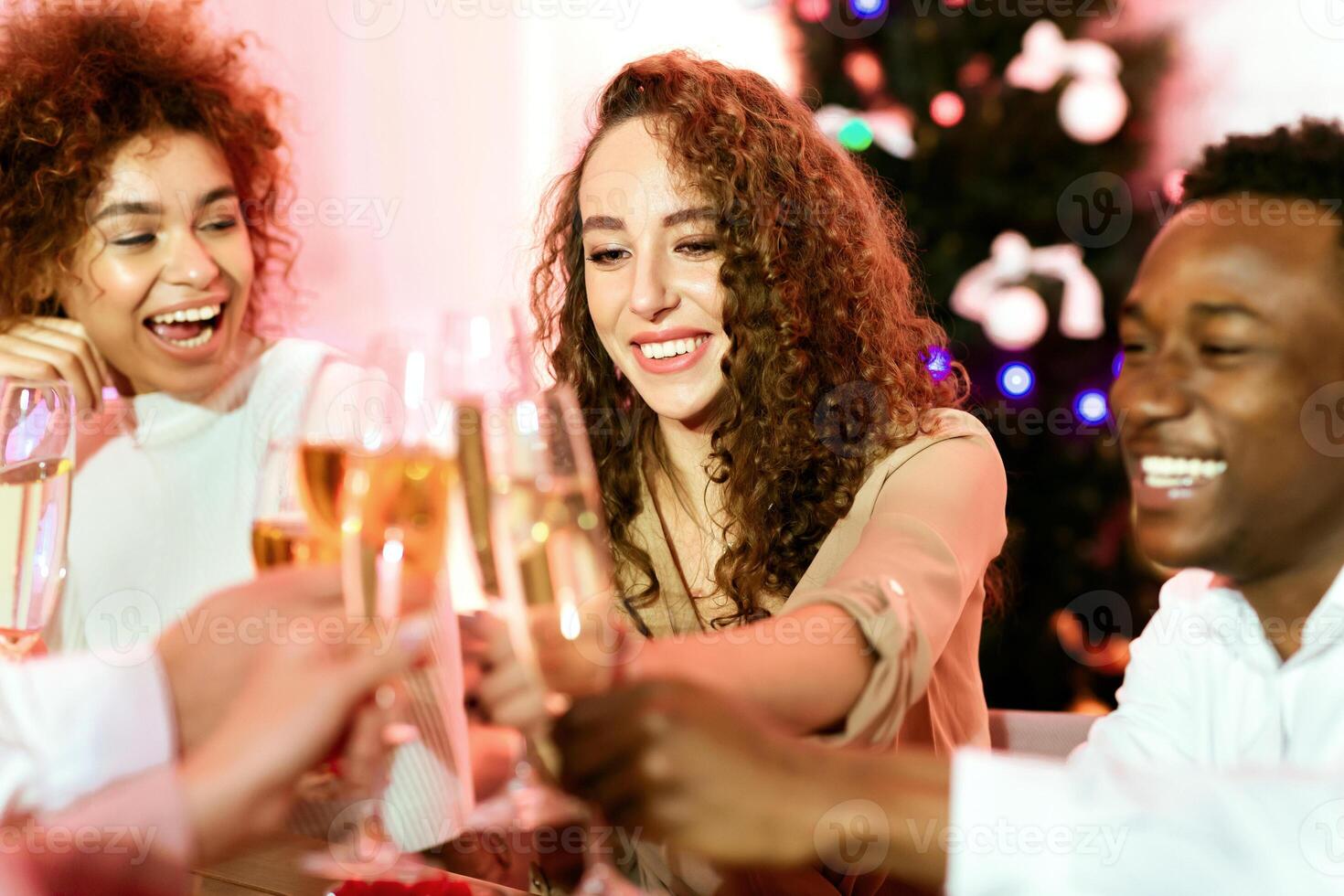 Multiracial Friends Celebrating New Year Together Clinking Glasses And Toasting Sitting At Table Indoors. Selective Focus photo