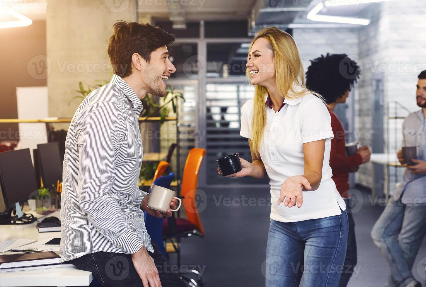 A man and a woman engaged in a conversation in an office setting. They are seated at a desk, with papers and a laptop in front of them, indicating a business discussion taking place. photo