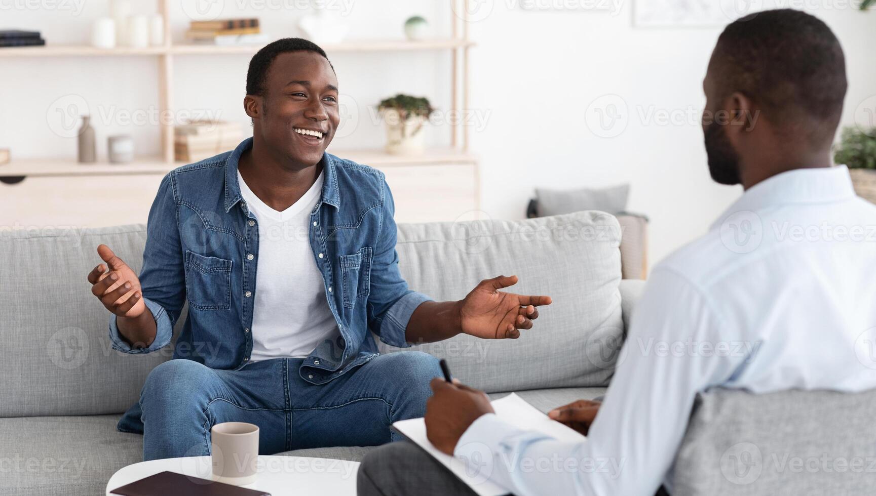 Successful Therapy. Cheerful black man talking to psychologist on meeting at his office, sharing his progress with doctor photo