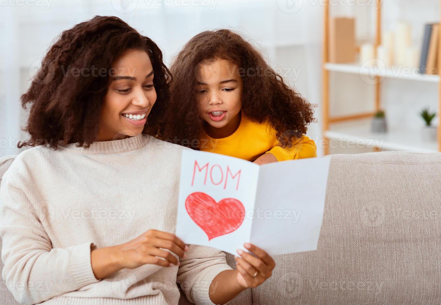 Mother's Day. Little Daughter Congratulating Mom Giving Greeting Card Celebrating Holiday Sitting Together On Couch At Home photo