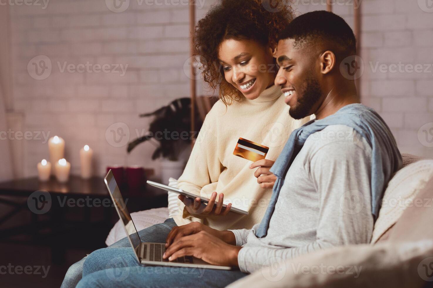 Happy afro couple doing internet shopping online on laptop, spending weekend at home photo