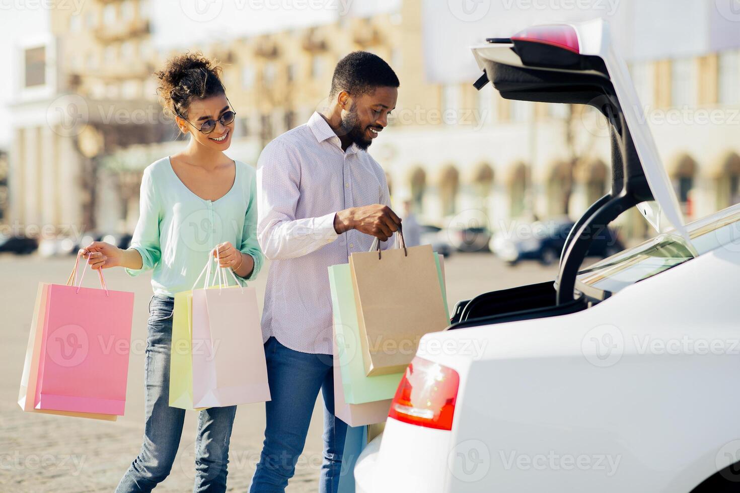 Black couple is loading shopping bags into the trunk of their car after a day of shopping. The woman is holding a pink shopping bag in her left hand and a multi-colored bag in her right. photo