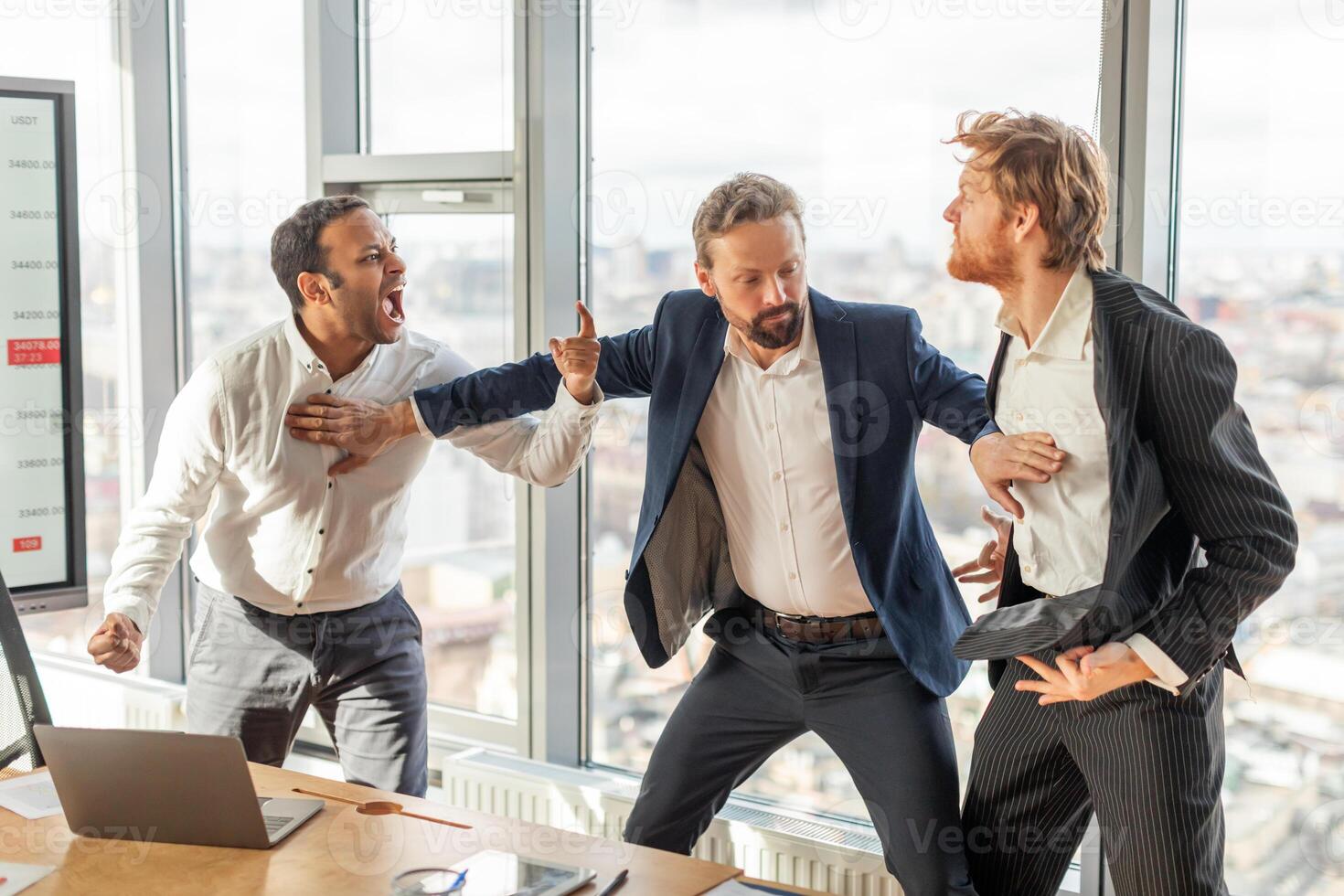 Three men in suits are arguing in a modern office with large windows. One man is pointing and yelling, while another man is gesturing with his hands. The third man is standing back and looking on. photo