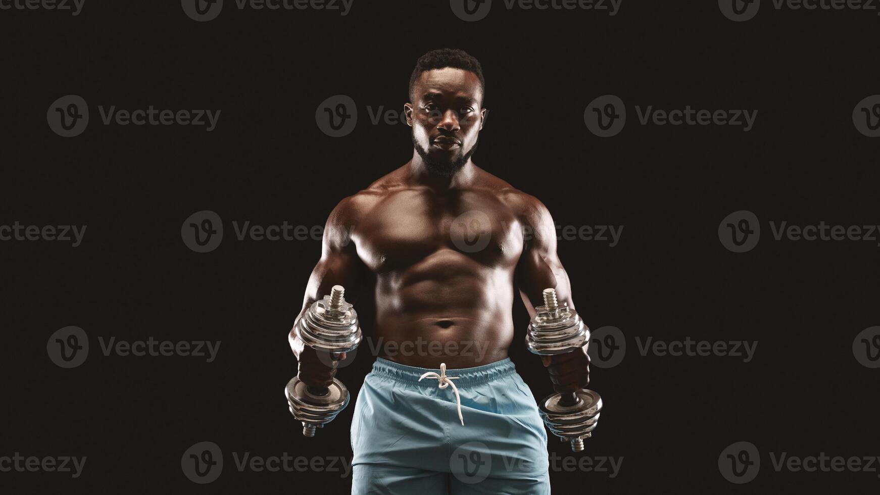 A muscular man lifts dumbbells while looking intensely at the camera. photo