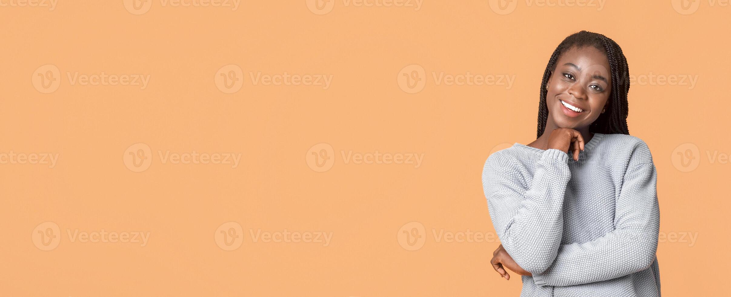 Interested black lady in blue sweater smiling over beige studio background, panorama with copy space photo