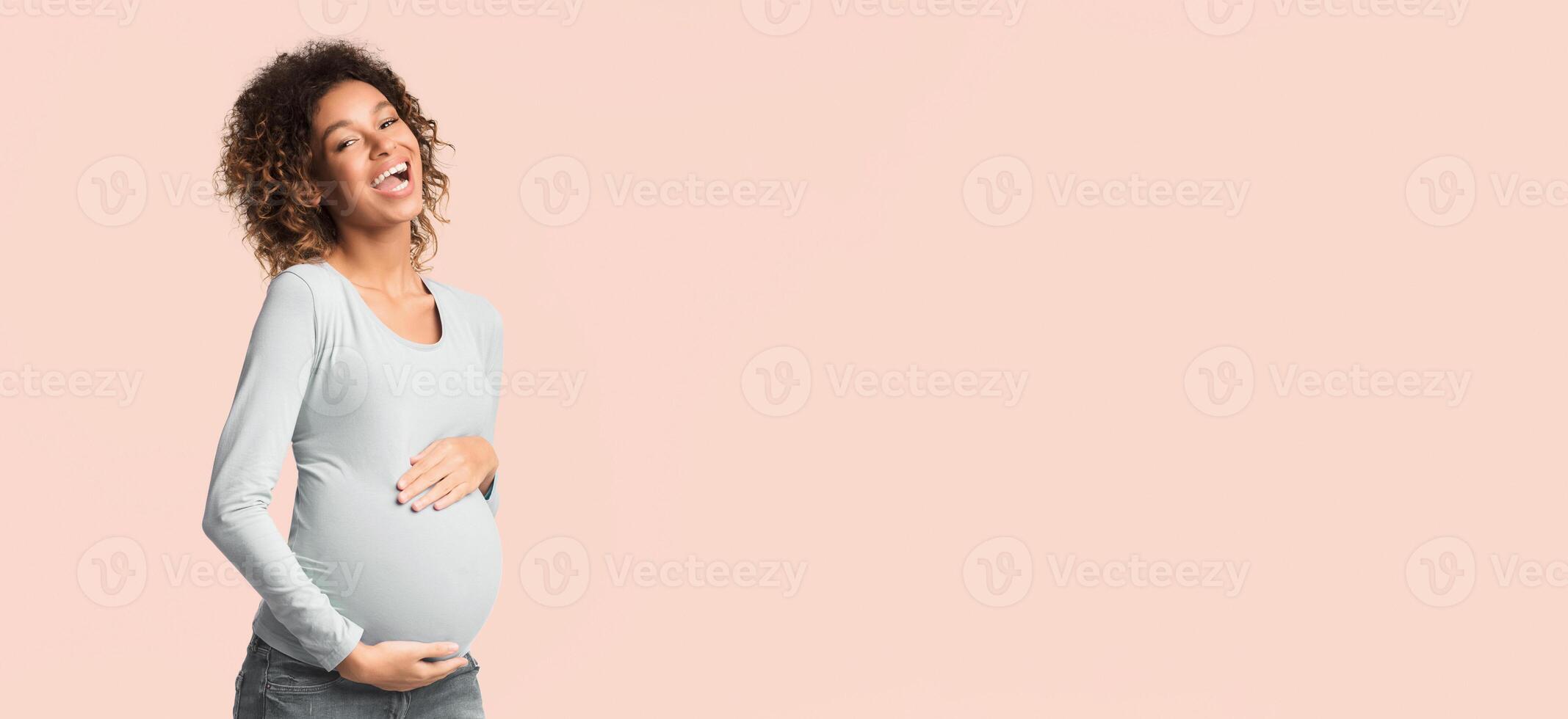 Excited african-american pregnant woman touching belly and laughing on white background photo