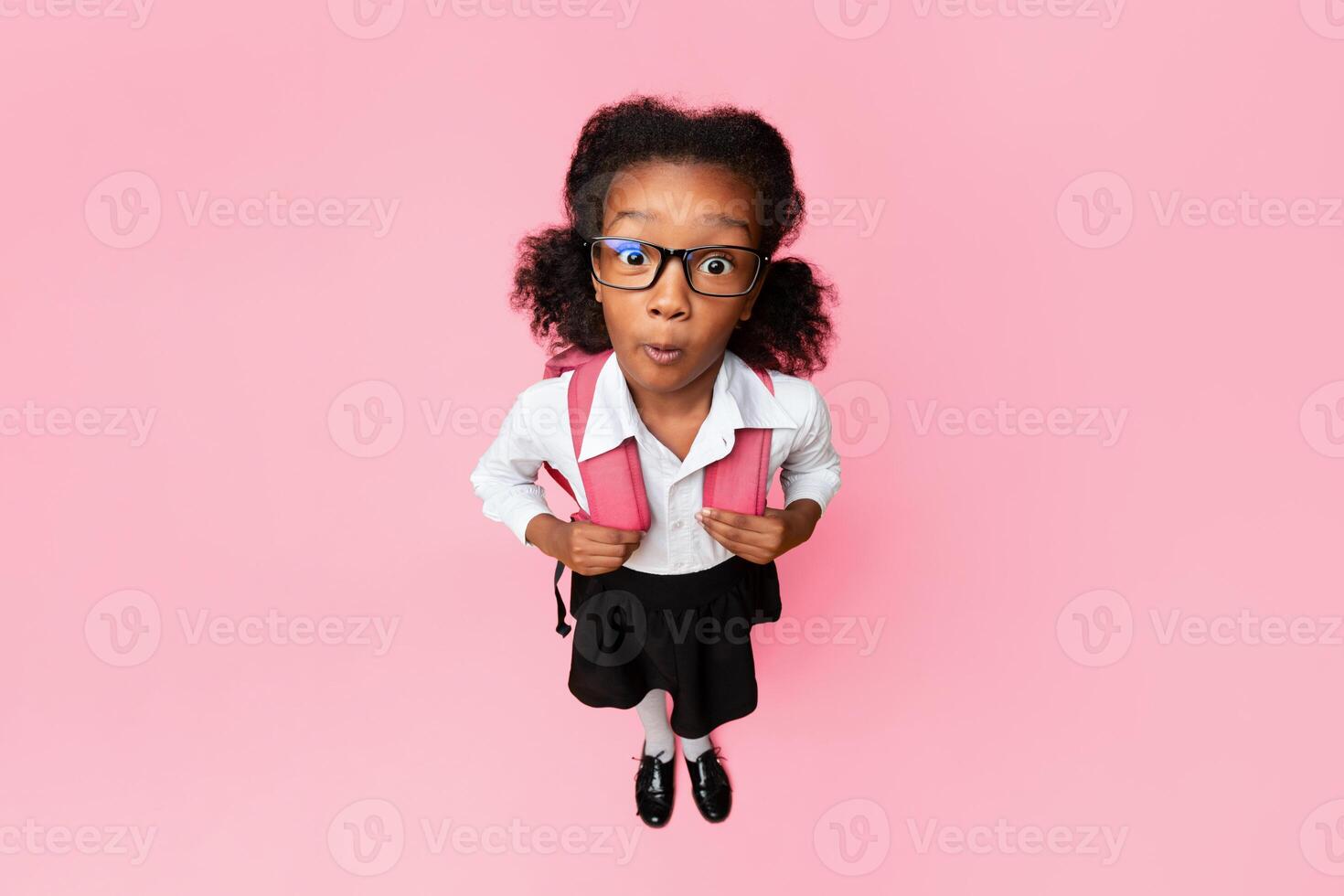Back To School Concept. Shocked Afro Girl Looking At Camera Posing In Studio. Yellow Background, High-Angle Shot photo