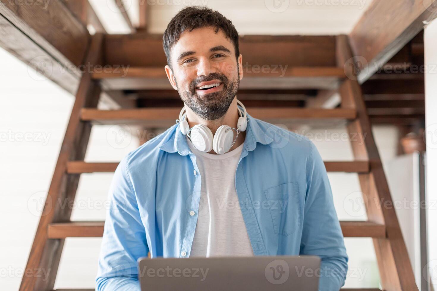 A man sitting with headphones on, focused on his laptop screen, typing and interacting with the digital device. He appears engaged in work or leisure activities. photo