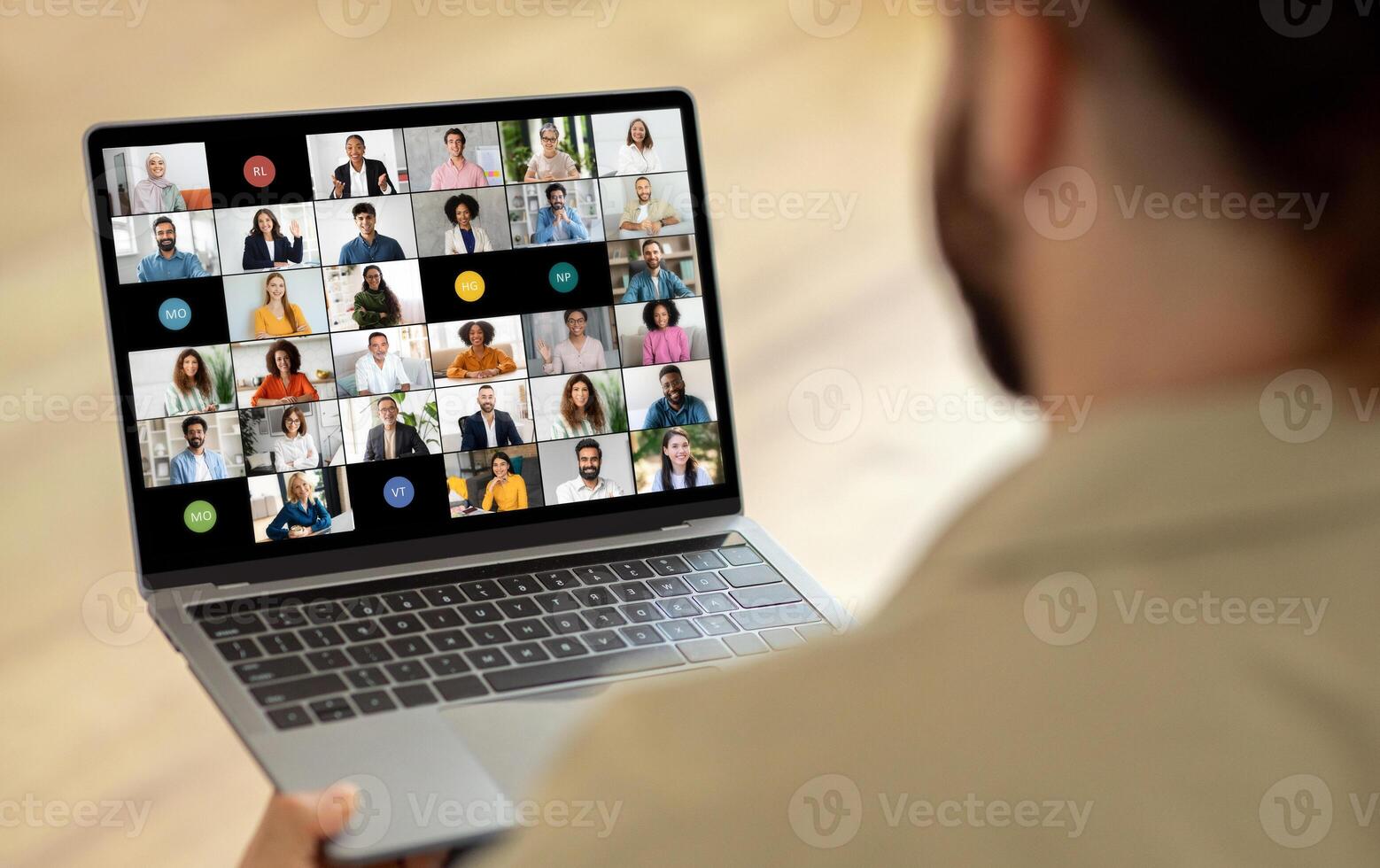 A man is seated in front of a laptop, where a screen displays a call with multiple people. He appears focused and engaged as he interacts with the group virtually. photo