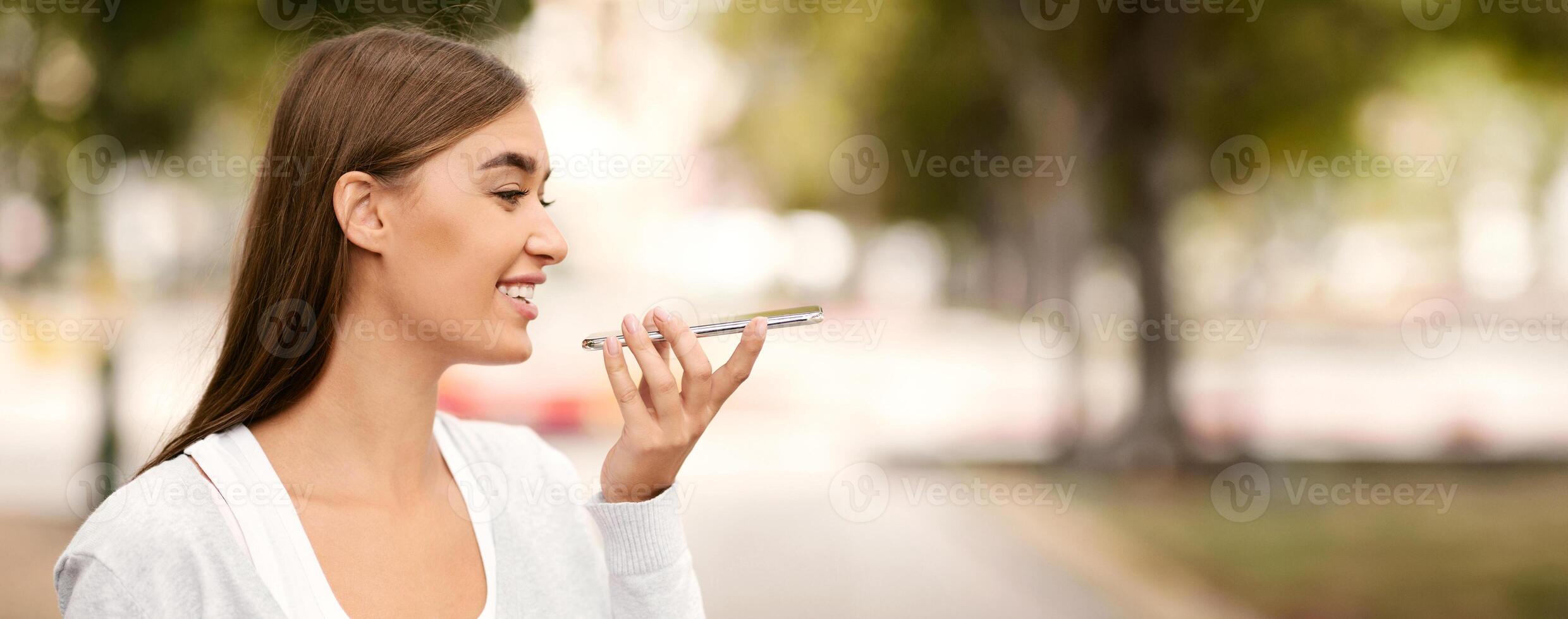 Smiling Girl Using Smartphone Voice Assistant Walking In Park Outdoors. Modern Life And Communication photo