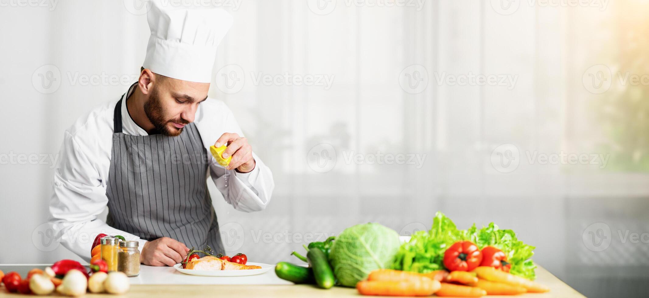 Chef Guy Cooking Fish Squeezing Lemon Juice On Roasted Salmon Steak Standing In Restaurant Kitchen. Selective Focus photo