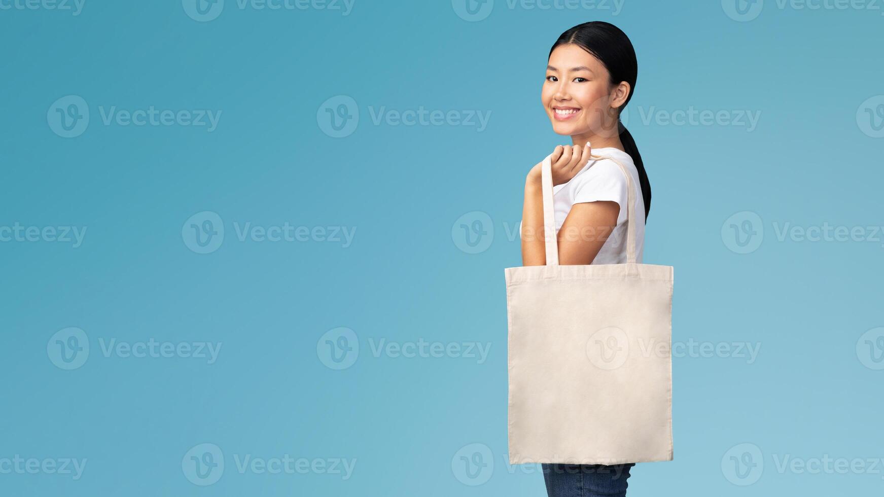 Ecology Concept. Asian Girl With White Eco Bag Smiling At Camera Standing On Blue Studio Background photo
