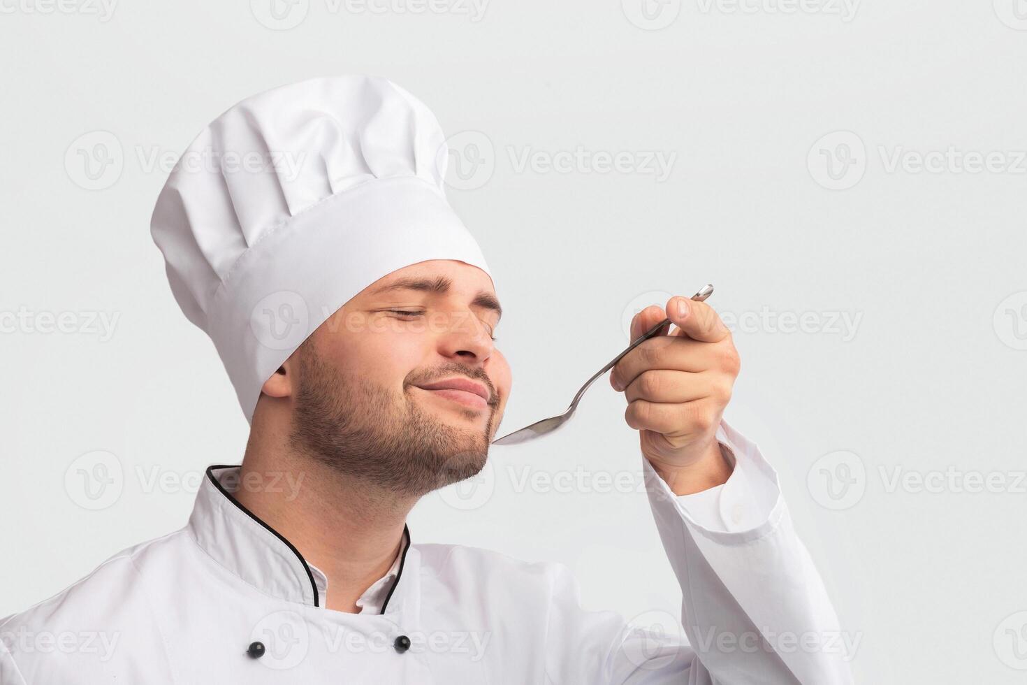 Culinary. Pleased Chef Man Tasting Food Holding Spoon Standing Over White Studio Background. Panorama, Free Space photo