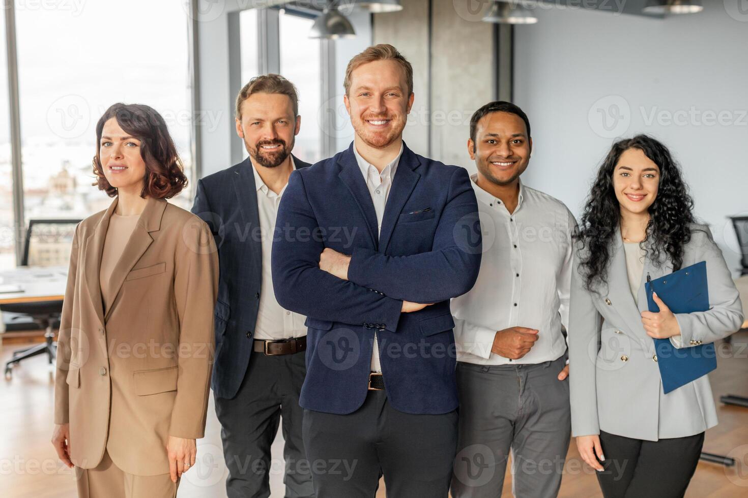 A diverse group of five business professionals stand together in a modern office setting. They are all wearing business attire and appear confident and successful. photo