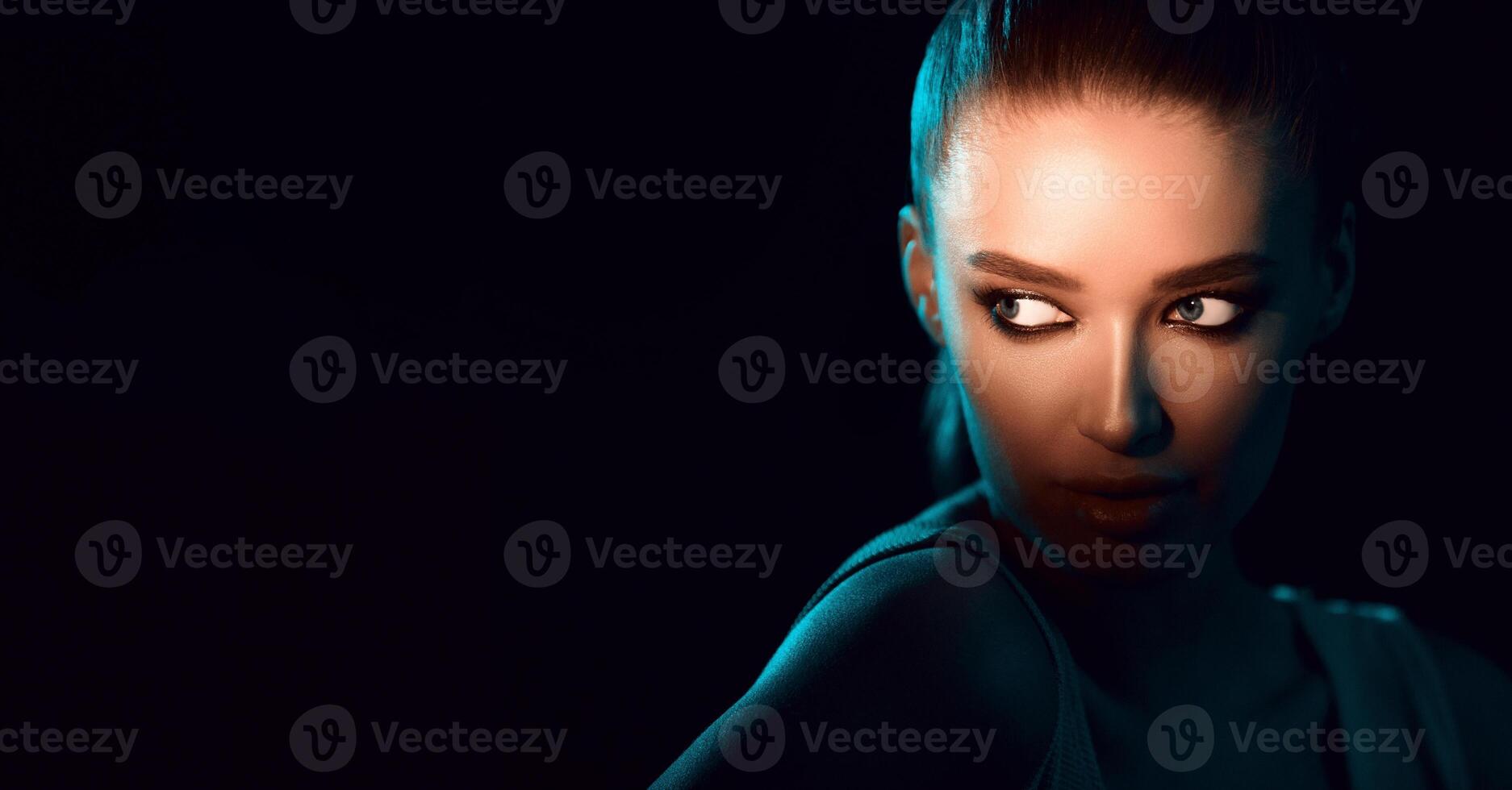 A woman is standing in the dark, her eyes fixed at copy space, with a somber expression on her face. The darkness around her adds an eerie atmosphere to the scene, panorama photo