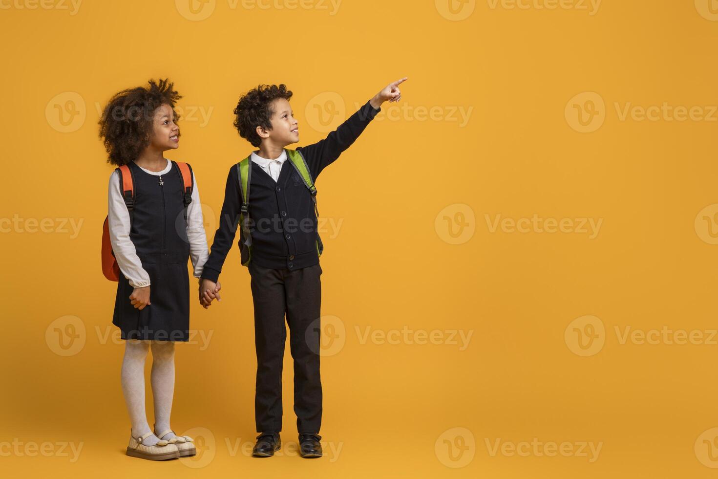 African American young boy and a girl schoolers are pointing at an indiscernible object or direction on yellow background. Their fingers are extended and they are looking intently at the same point. photo