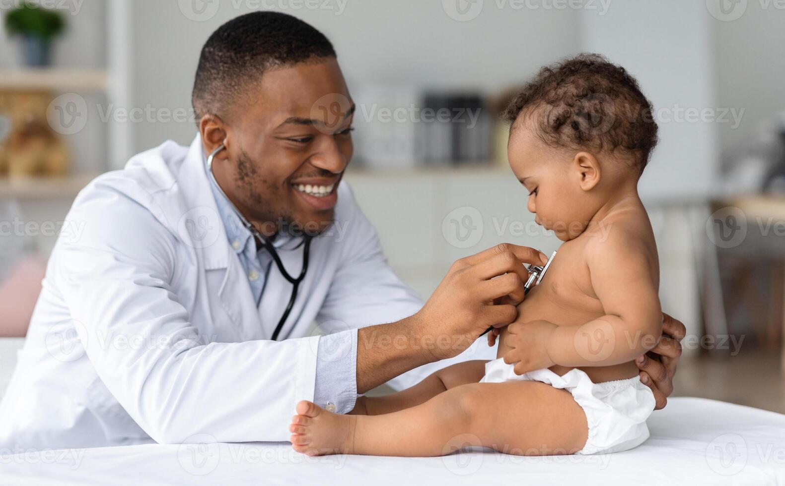 Black Pediatrician Doctor Doing Check Up To Cute Newborn Baby In Diaper, African American Pediatrist Using Stethoscope For Listening Child's Heartbeat, Checking Infant's Heart And Lungs In Clinic photo