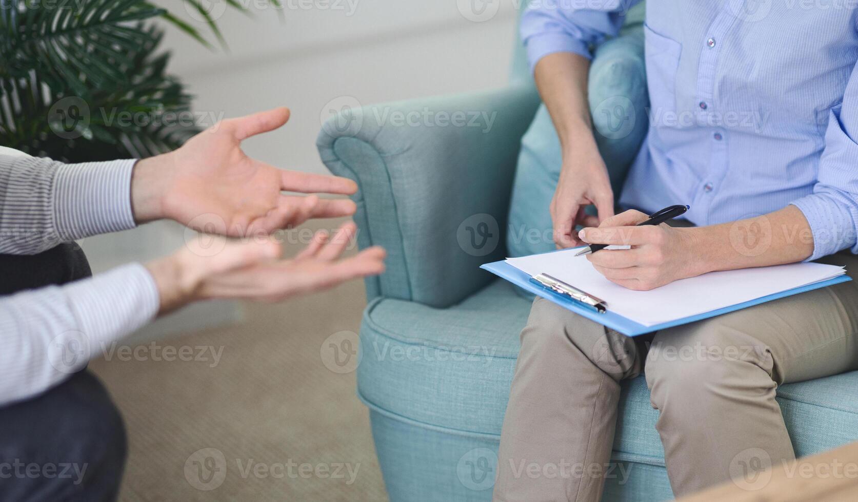 Cropped of therapist actively listens while taking notes on a clipboard, during a counseling session with man in a modern office on a sunny afternoon photo