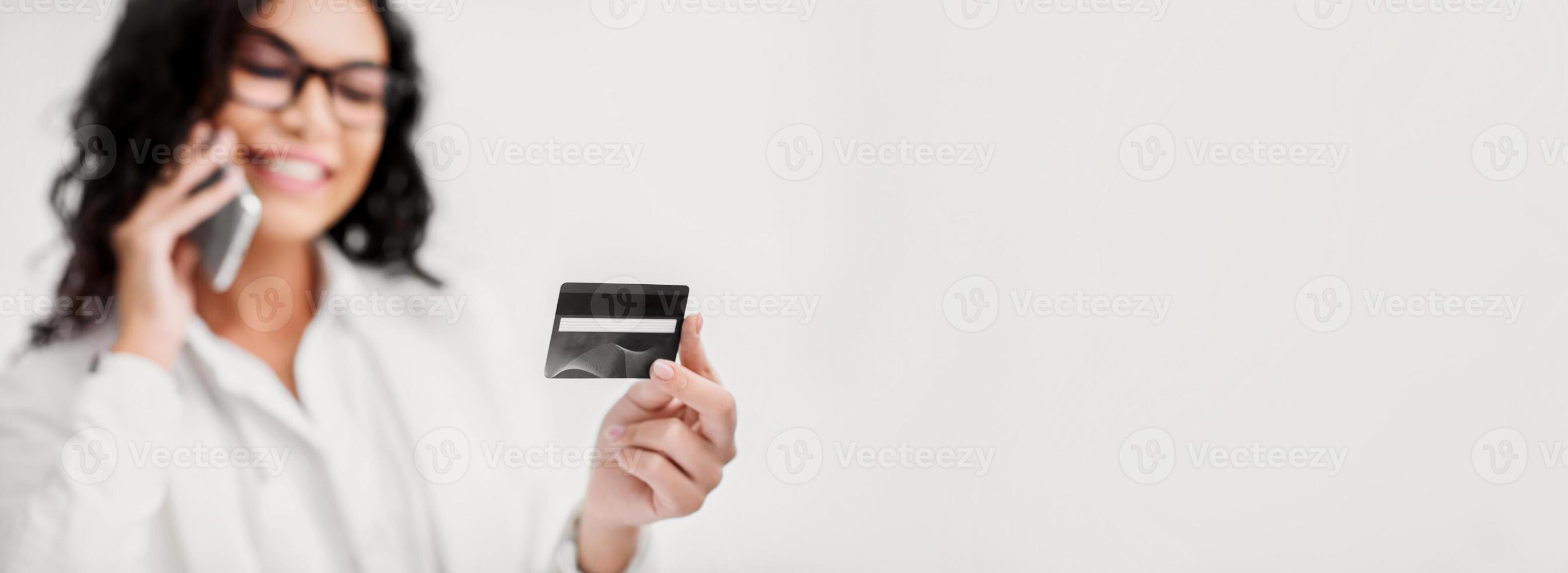 Shopping Online. Hispanic woman holding credit card, talking on cell phone. Copy space, selective focus photo