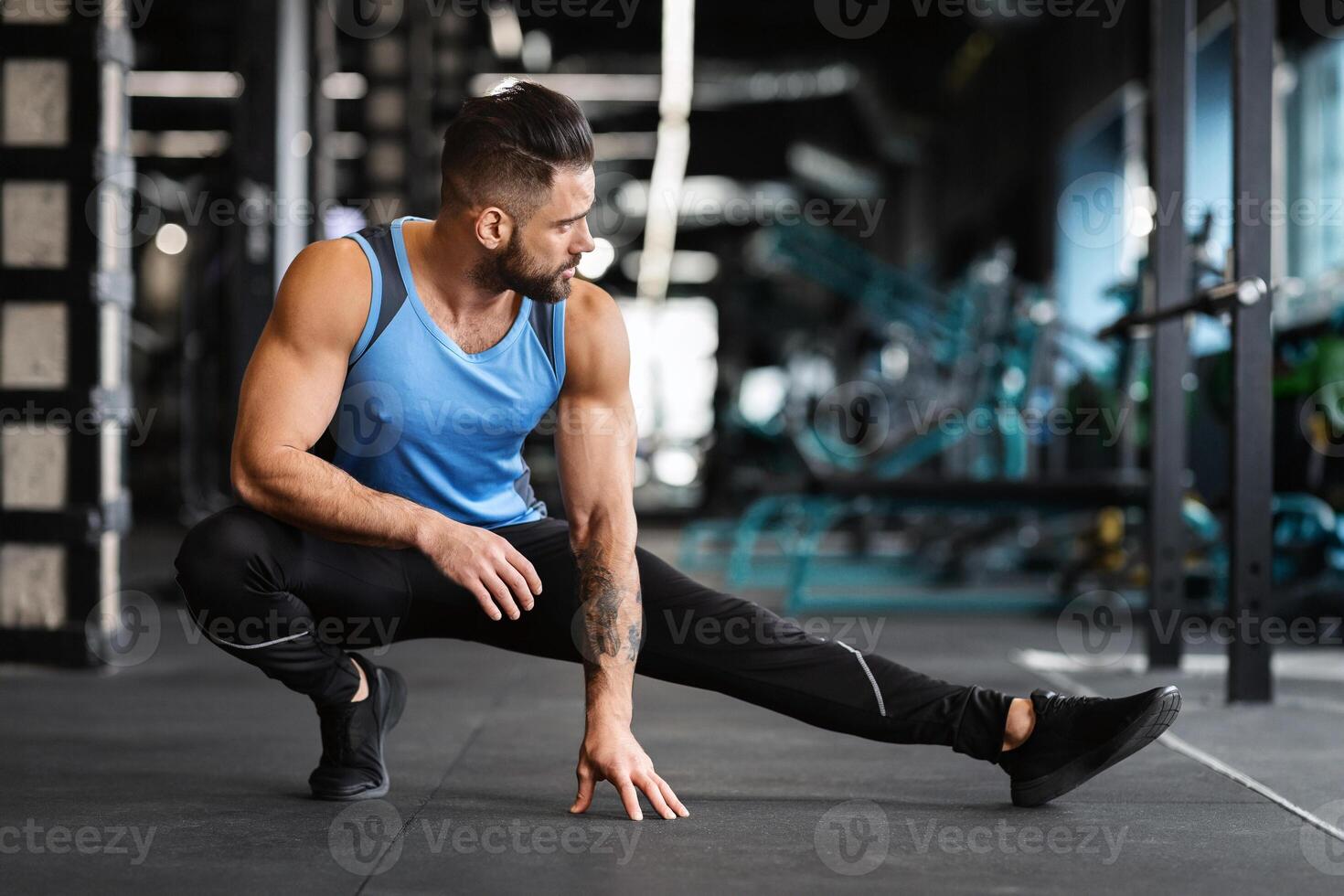 Sporty man at gym doing stretching exercises for legs, empty space photo