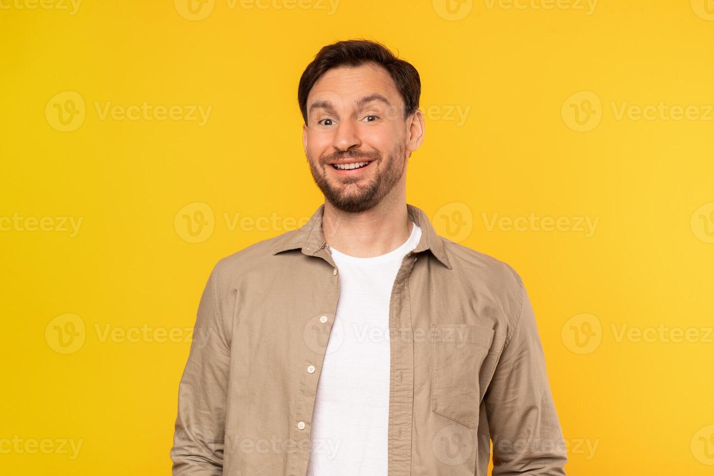 A man is standing upright in front of a bright yellow background. He appears to be looking straight ahead, with his hands by his sides, smiling at camera photo
