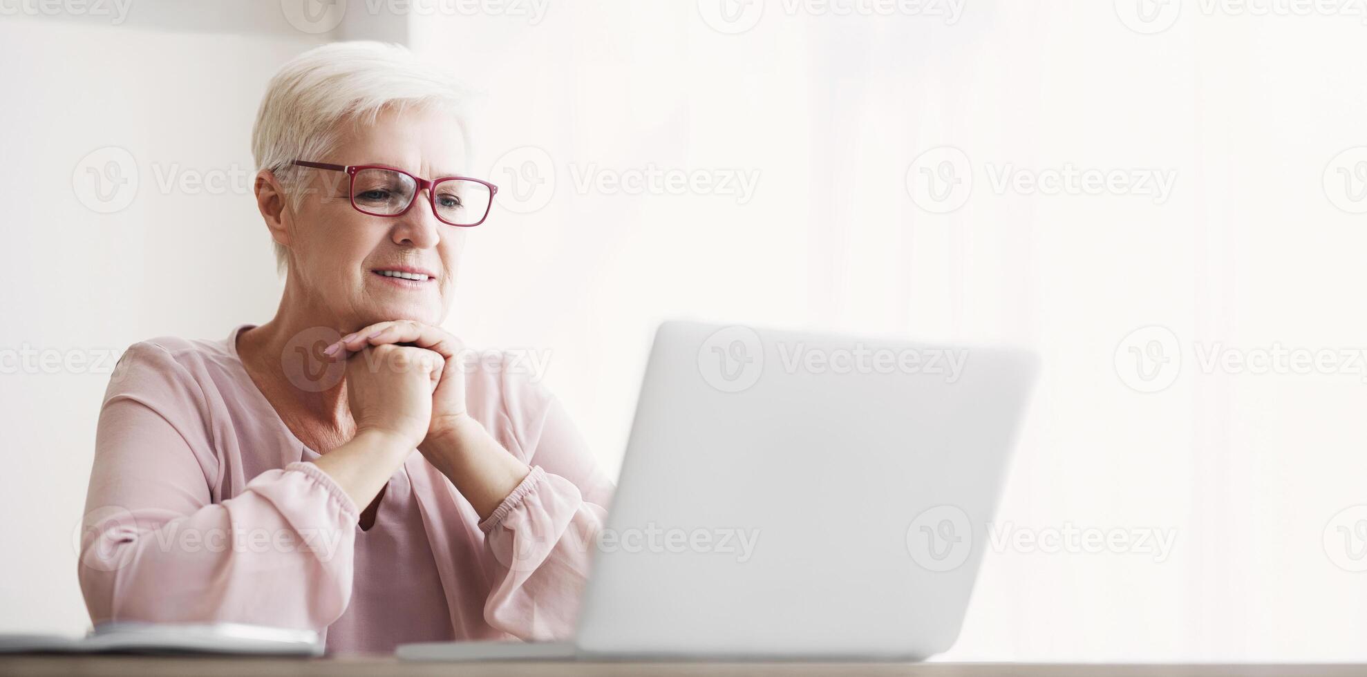 Senior excited woman reading article online, using laptop at home, free space photo