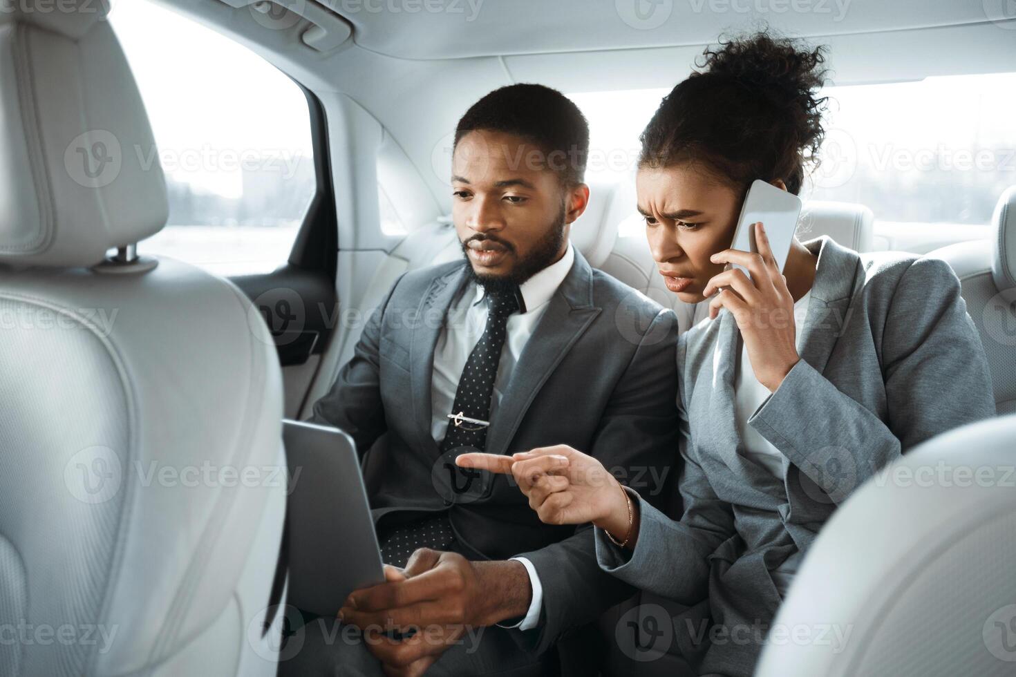 African American man and woman in business attire are working in a car. They are both focused on their work, which suggests they are serious and dedicated to their business. photo