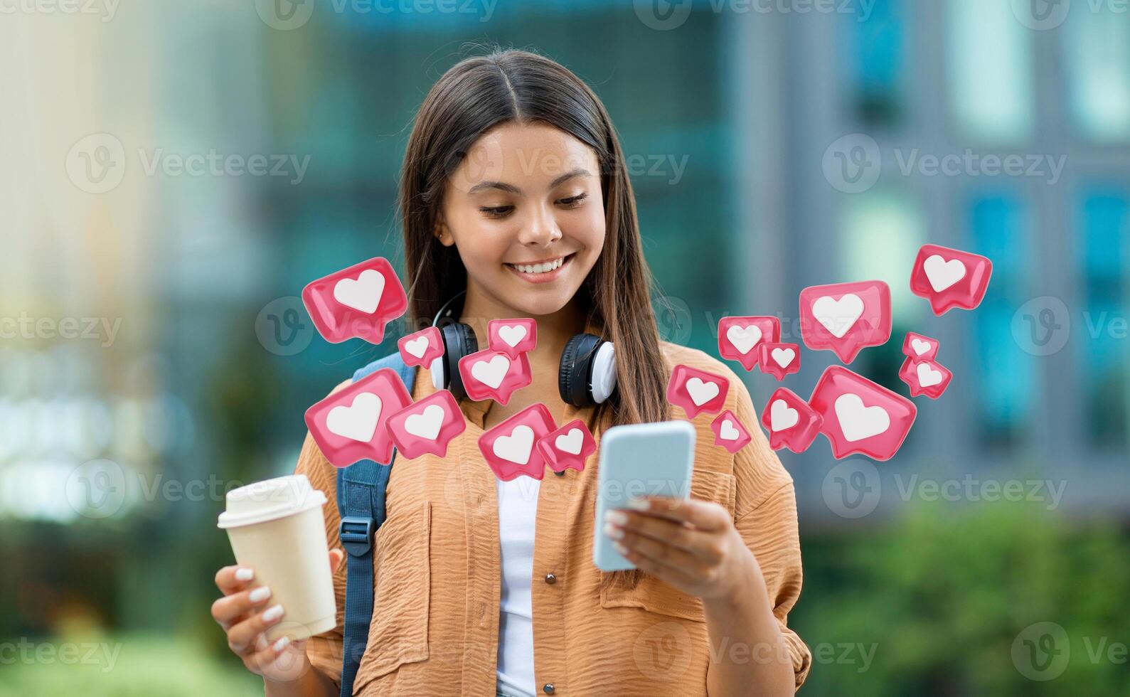 A young woman smiles as she uses her smartphone. Social media icons in the shape of hearts are surrounding her, symbolizing the popularity of the content she is creating or viewing photo