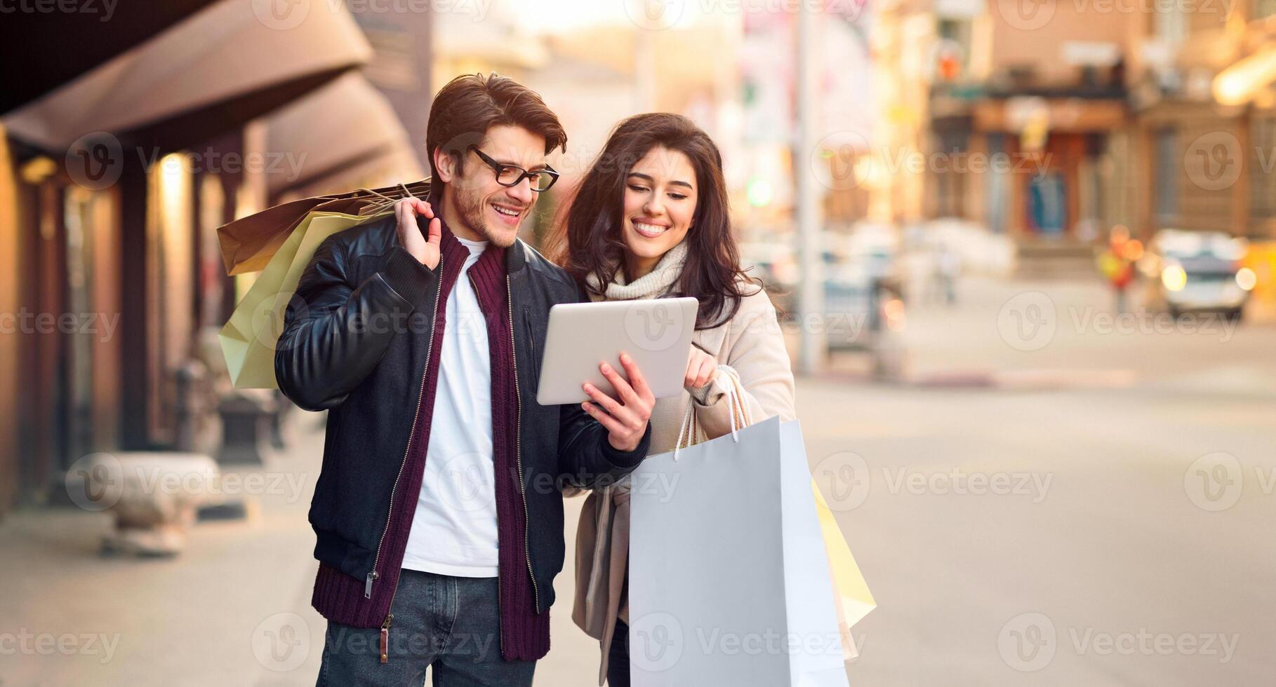 A man and woman holding shopping bags while looking at a tablet computer together. photo
