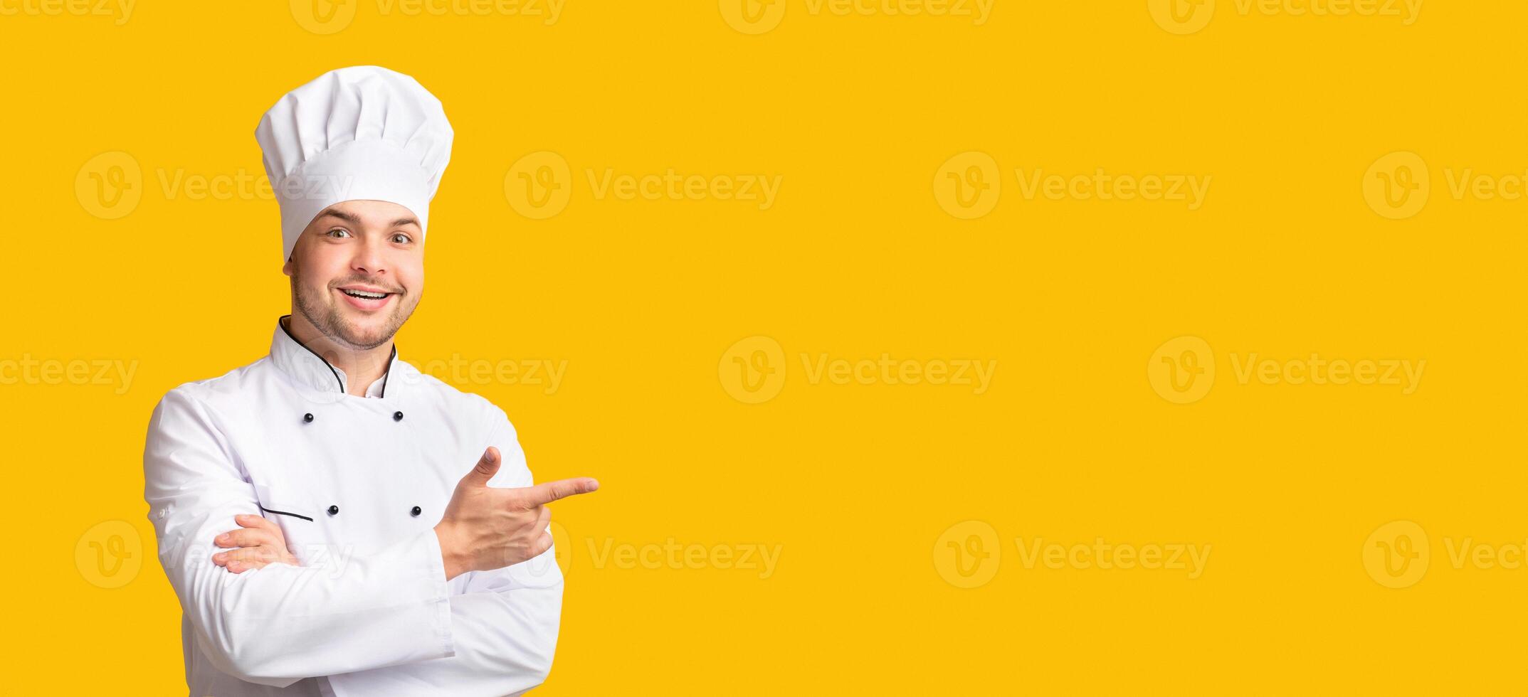 Look There. Male Chef Pointing Fingers Aside Standing On Yellow Studio Background. Panorama, Free Space For Text photo