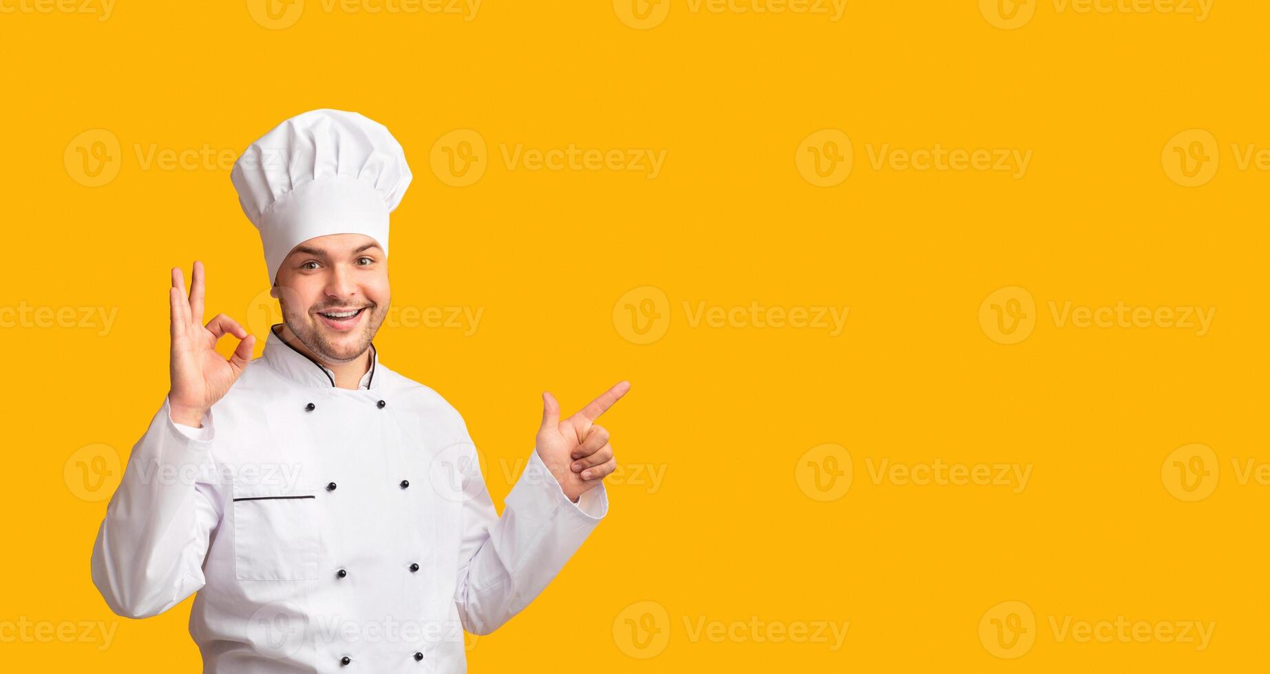 Smiling Chef Man Gesturing Okay Pointing Finger At Copy Space Approving Something Posing Over Yellow Studio Background. Panorama photo