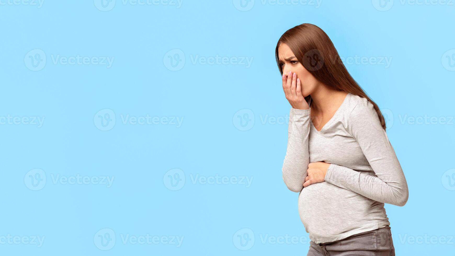 Pregnancy Morning Sickness. Pregnant Woman Having Nausea Feeling Bad And Sick Standing Over Gray Background. Studio Shot, Panorama, Copy Space photo