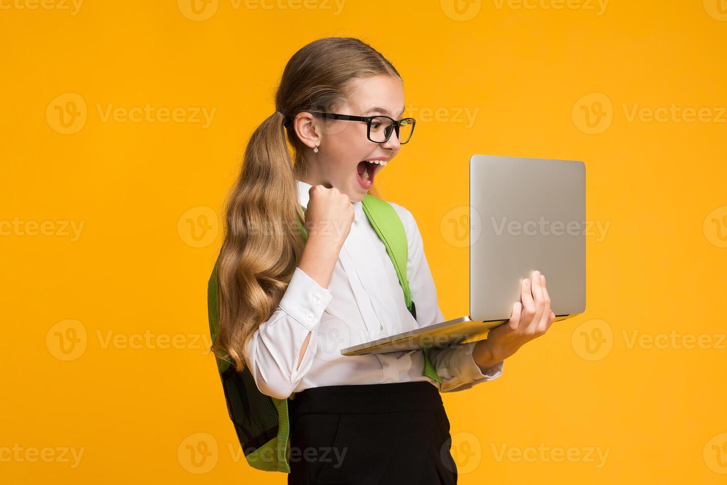 Computer Game Addiction. Overjoyed School Girl Playing Computer Games On Laptop Over Yellow Background In Studio. Free Space For Text photo