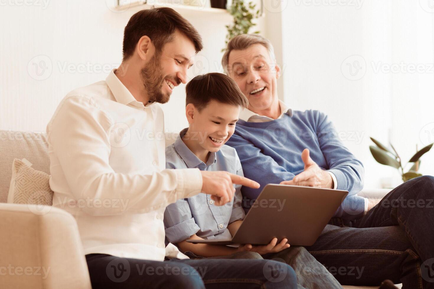 Happy Boy Using Laptop Sitting Between Father And Grandfather, Laughing And Having Fun Together On Couch At Home. Selective Focus photo