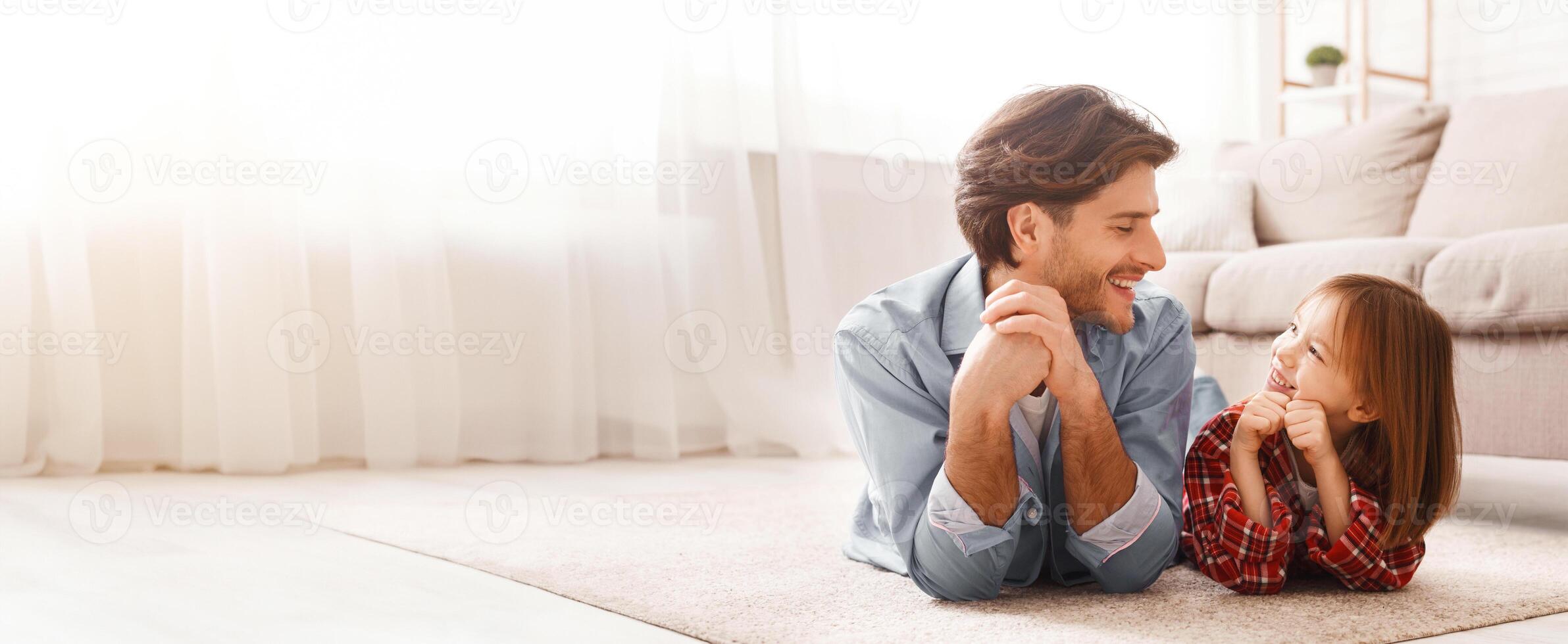 Cheerful daddy and his liitle daughter laying on floor and looking at each other, lets have fun, home interior, free space photo