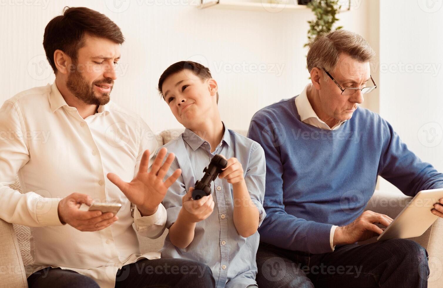 Indifference. Busy Father And Grandfather Refusing To Play Game With Boy Siitting On Sofa Indoor. Selective Focus photo