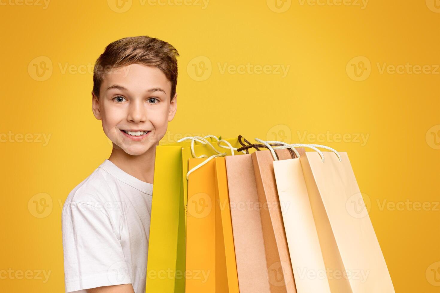 Cheerful teen boy holding lots of shopping bags and smiling, orange studio background photo