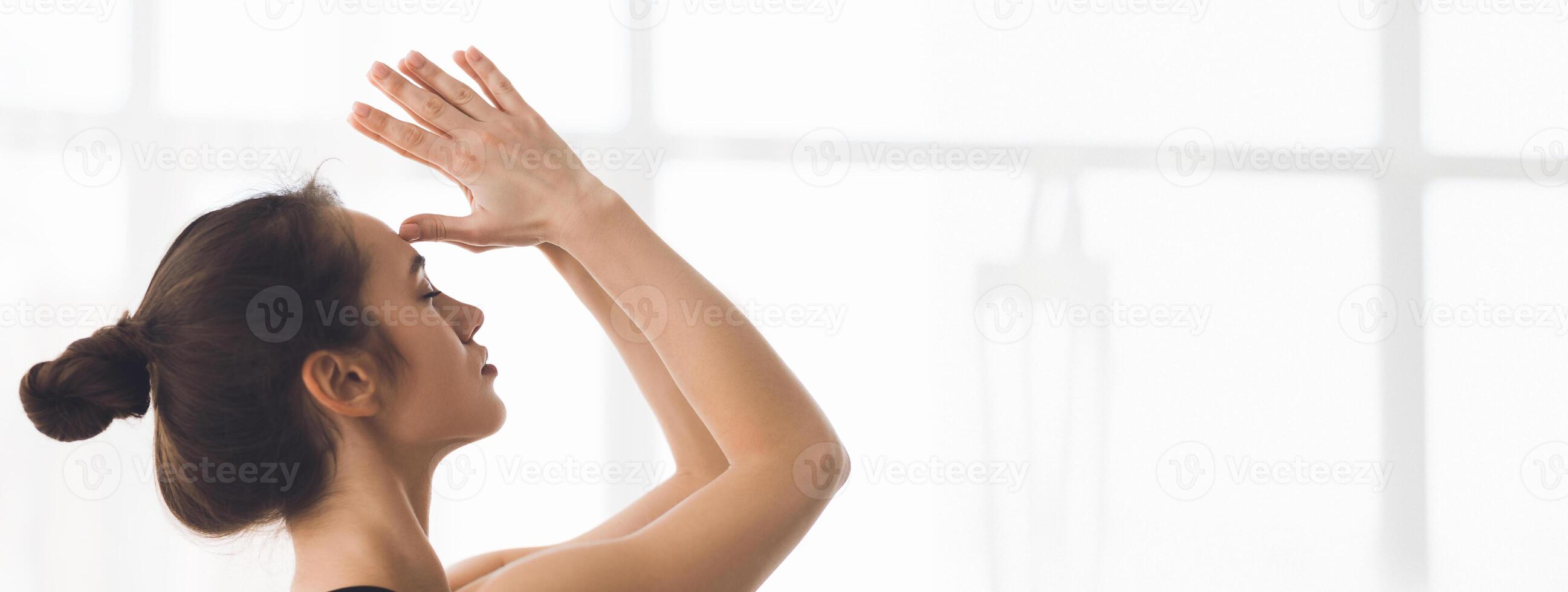 A young woman is practicing yoga indoors, reaching her arm overhead while enjoying the soft morning light filtering through the windows, copy space photo